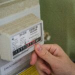 A person's hand pointing at the digital display of a utility meter, symbolizing energy consumption monitoring and bill management.