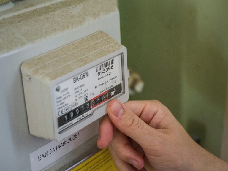 A person's hand pointing at the digital display of a utility meter, symbolizing energy consumption monitoring and bill management.